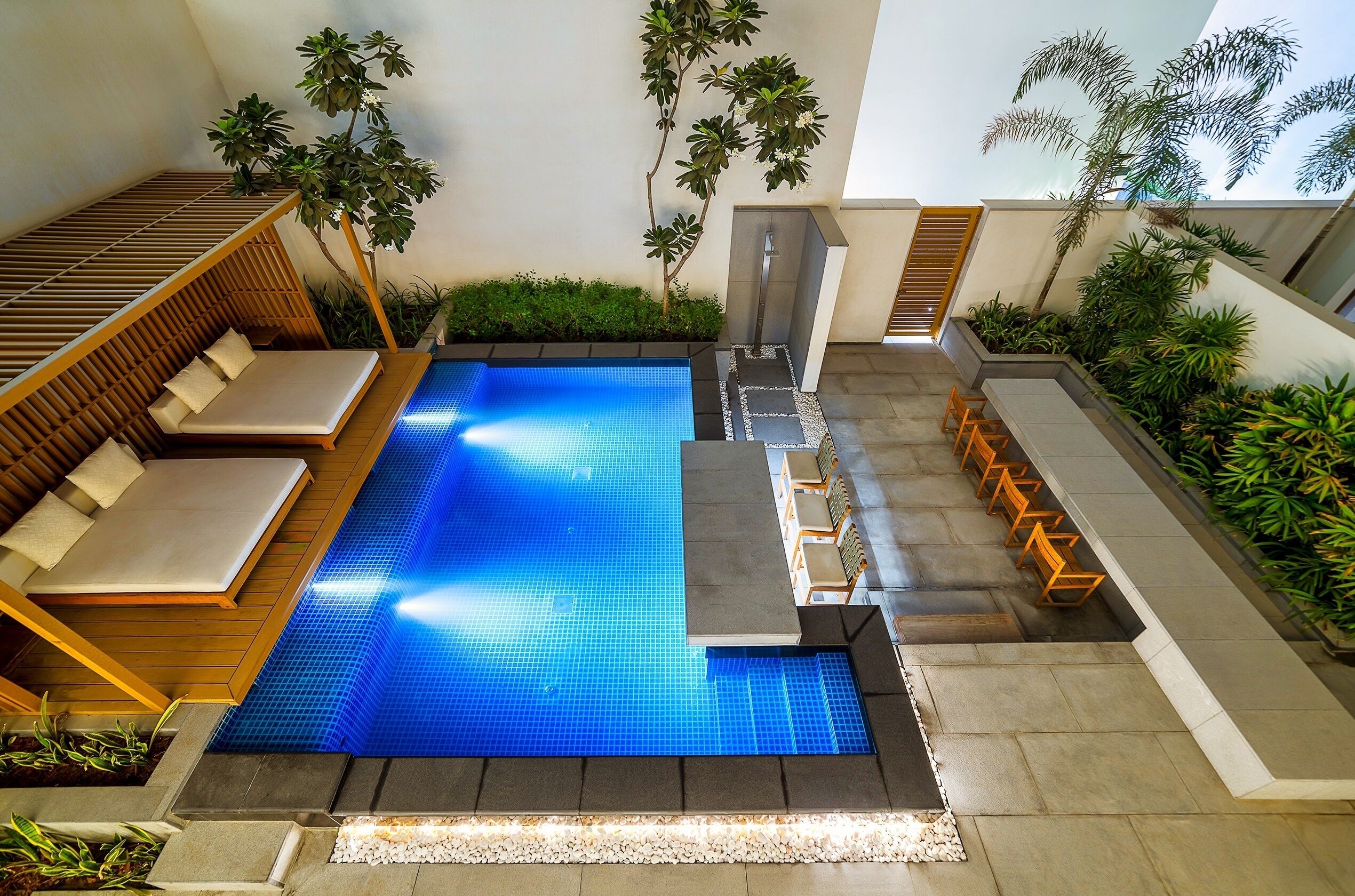 A modern outdoor swimming pool with a sun lounger, seating area, and a small waterfall feature.