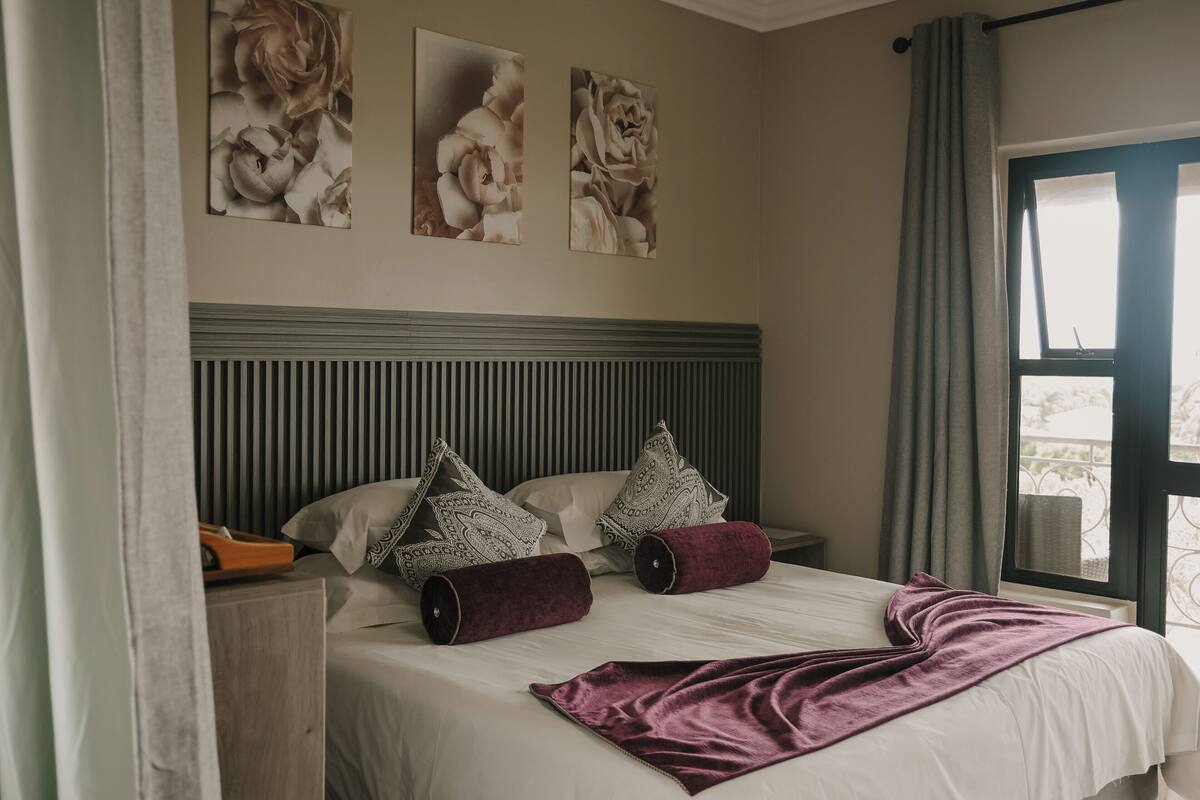 A bedroom with a bed, pillows, a blanket, and wall art.