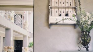 A hotel lobby with a checkered floor, a white dresser with drawers, and a decorative wall-mounted shelf with a vase of flowers. - Stone Olive Guest House (Jeffreys Bay)