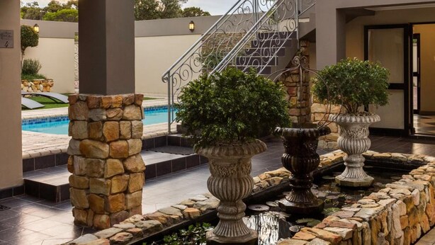 A modern building with a stone facade, a pool, and a staircase leading to the upper level. - Stone Olive Guest House (Jeffreys Bay)
