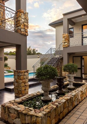 A modern building with a stone facade, a pool, and a staircase leading to the upper level. - Stone Olive Guest House (Jeffreys Bay)