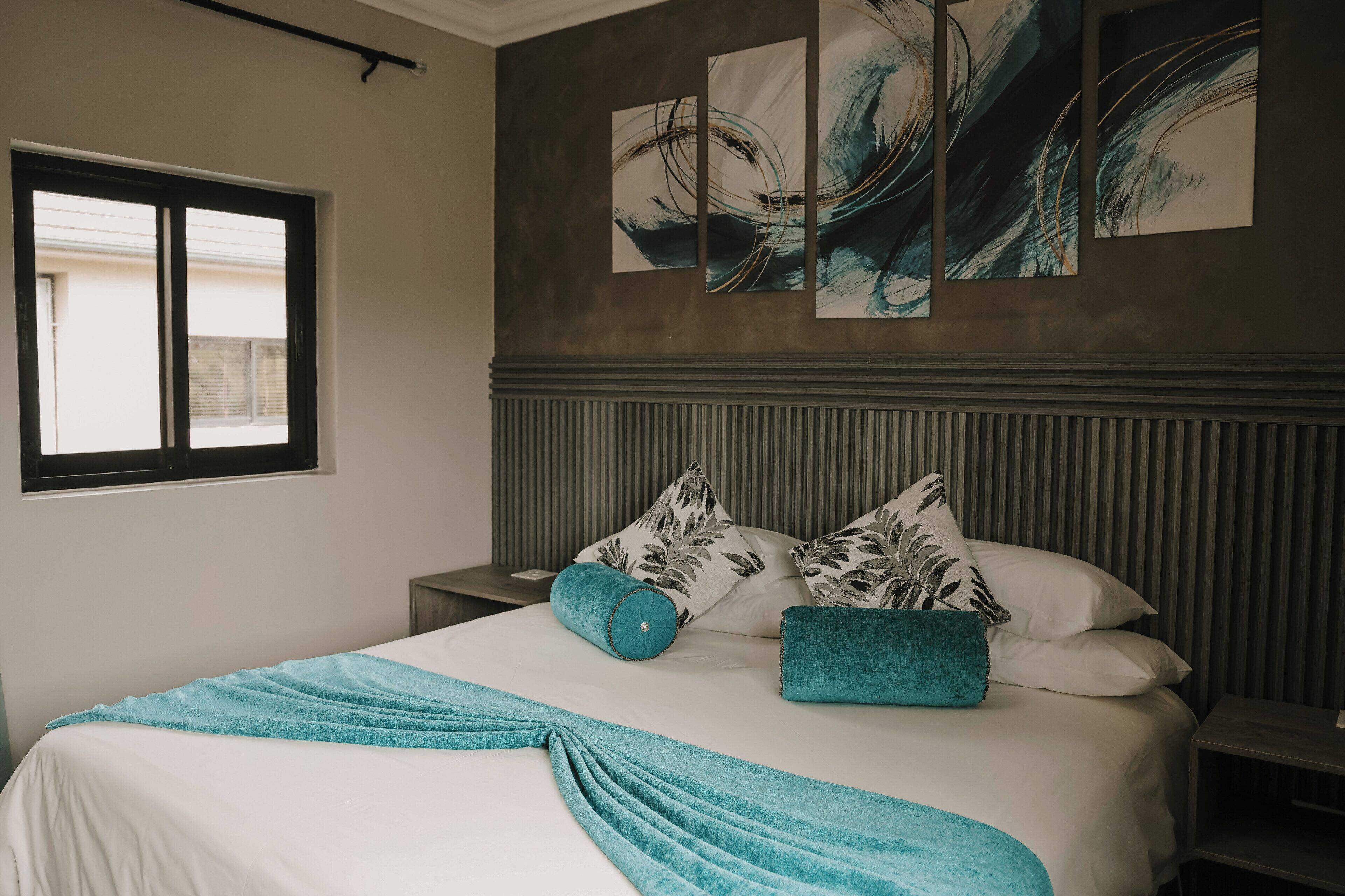 A neatly made bed with a teal throw blanket, a pillow with a teal accent, and a headboard with abstract art.