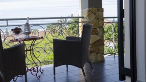 A balcony with wicker furniture and a table set with a pitcher and glasses, overlooking a scenic view. - Stone Olive Guest House (Jeffreys Bay)