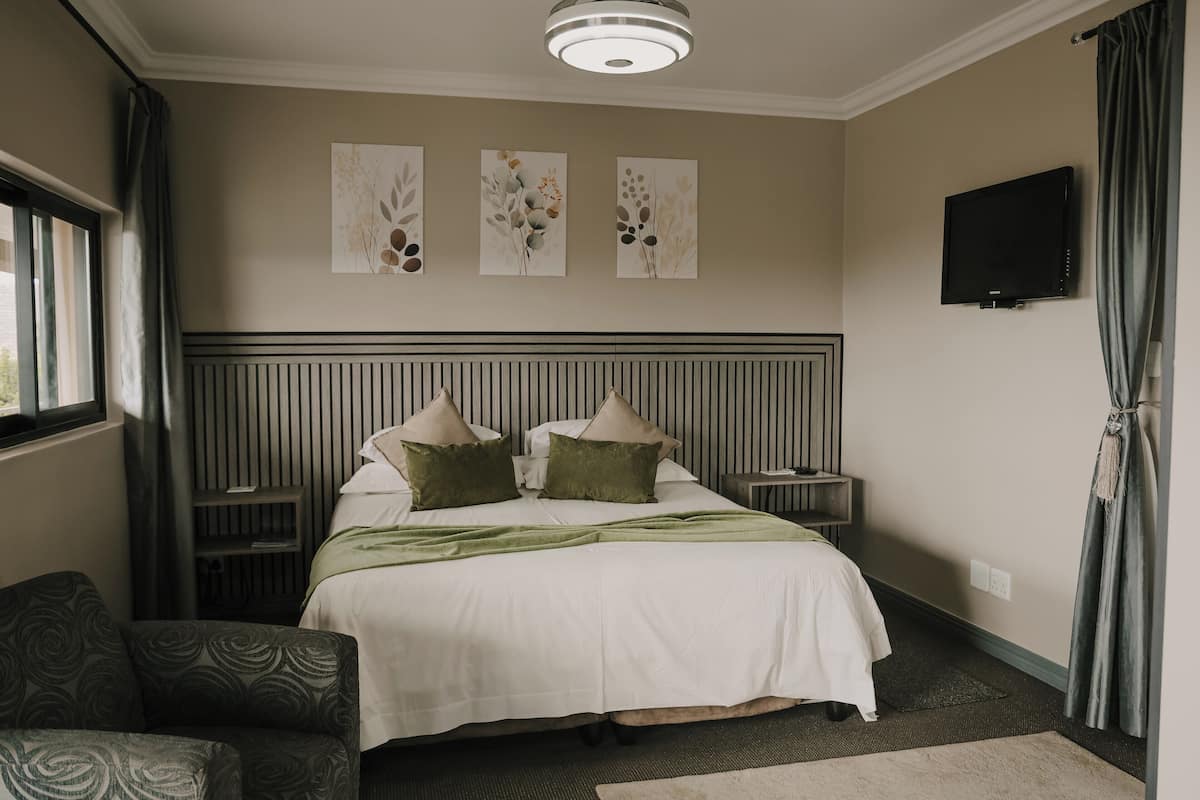 A hotel room with a bed, two nightstands, a TV, and artwork on the wall.