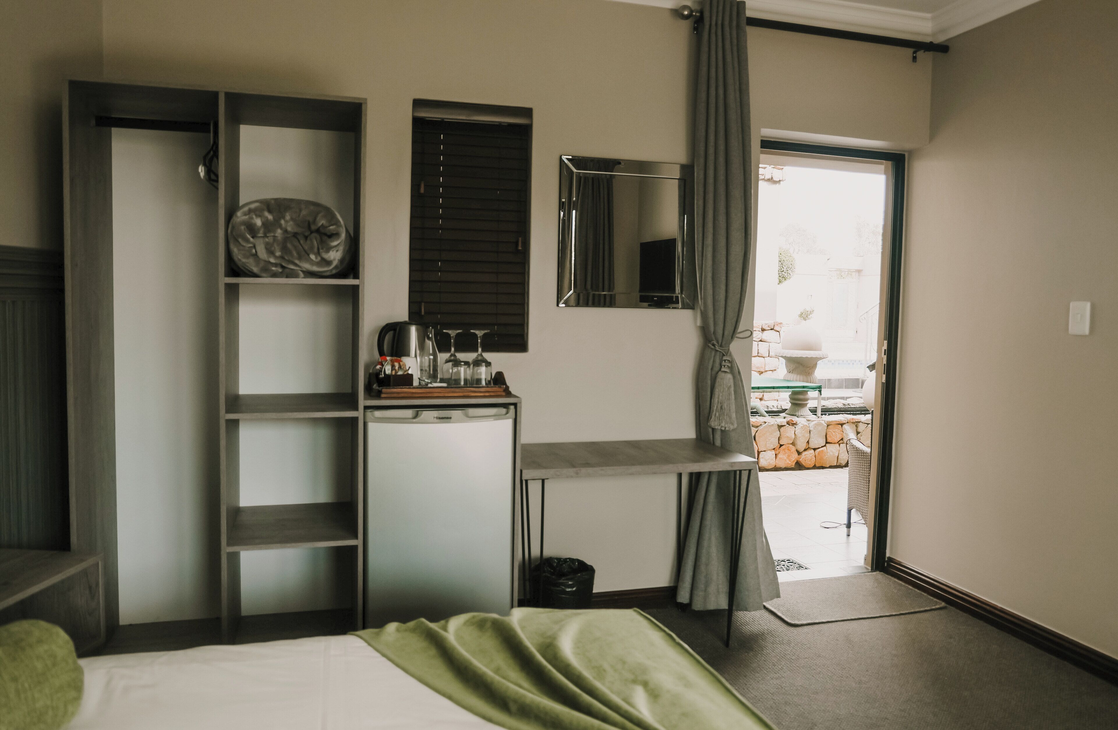 Habitación de hotel con cama, escritorio con espejo, estanterías y vistas al exterior.