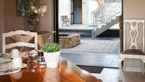 A dining area with a wooden table set for two, a vase with flowers, and a view of a pool and staircase leading outside. - Stone Olive Guest House (Jeffreys Bay)