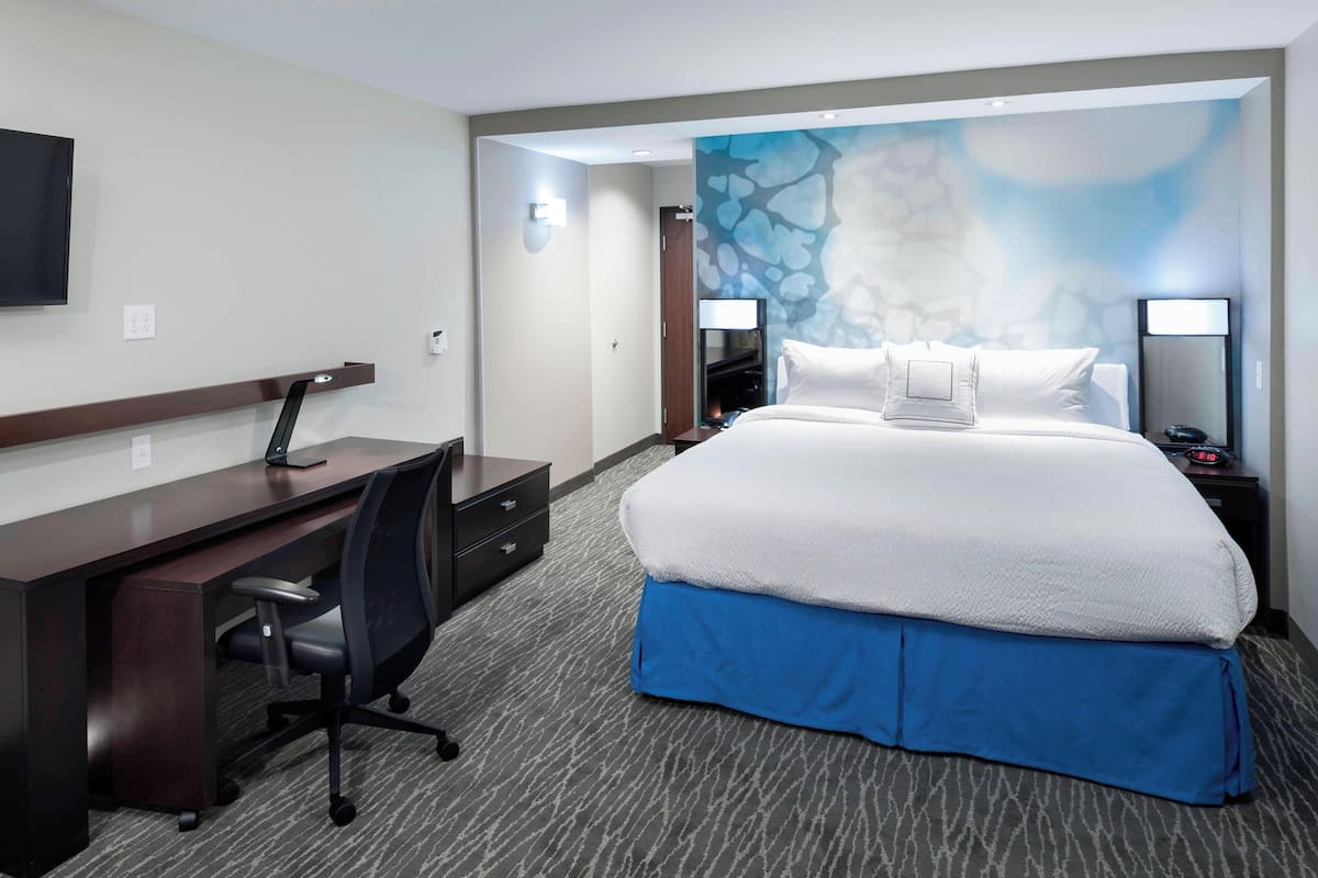 A hotel room with a bed, desk, chair, and a TV.
