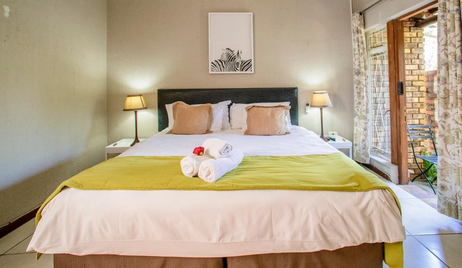 A neatly made bed with a green and white bedspread, two bedside lamps, and a framed artwork on the wall.