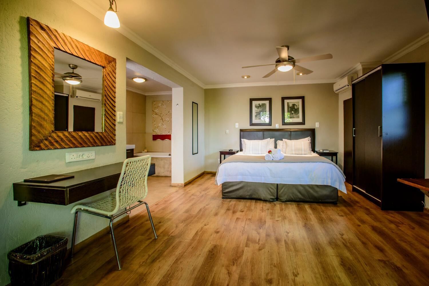 A hotel room with a bed, a desk, a chair, a ceiling fan, and a large mirror.
