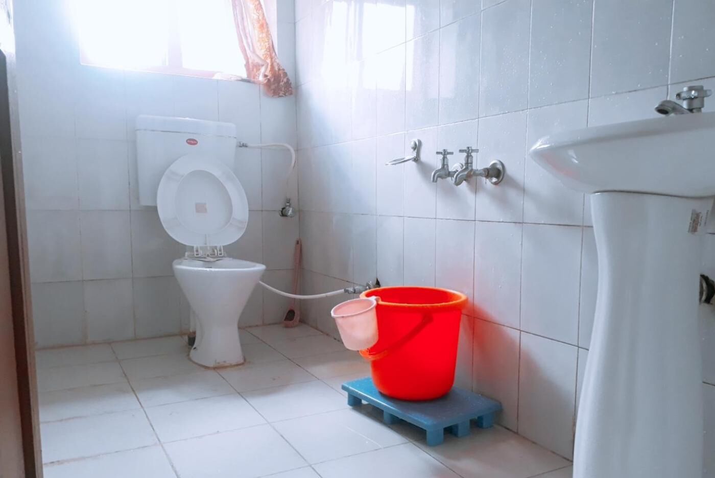 Ein Badezimmer mit Toilette, Waschbecken und einem roten Eimer auf einem blauen Hocker.