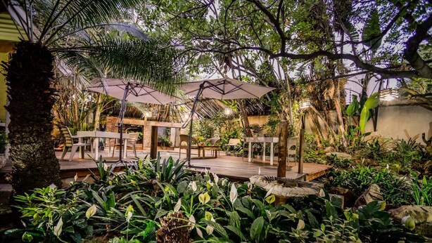 Un patio al aire libre con mesas y sillas de madera, rodeado de exuberante vegetación y una terraza de madera.