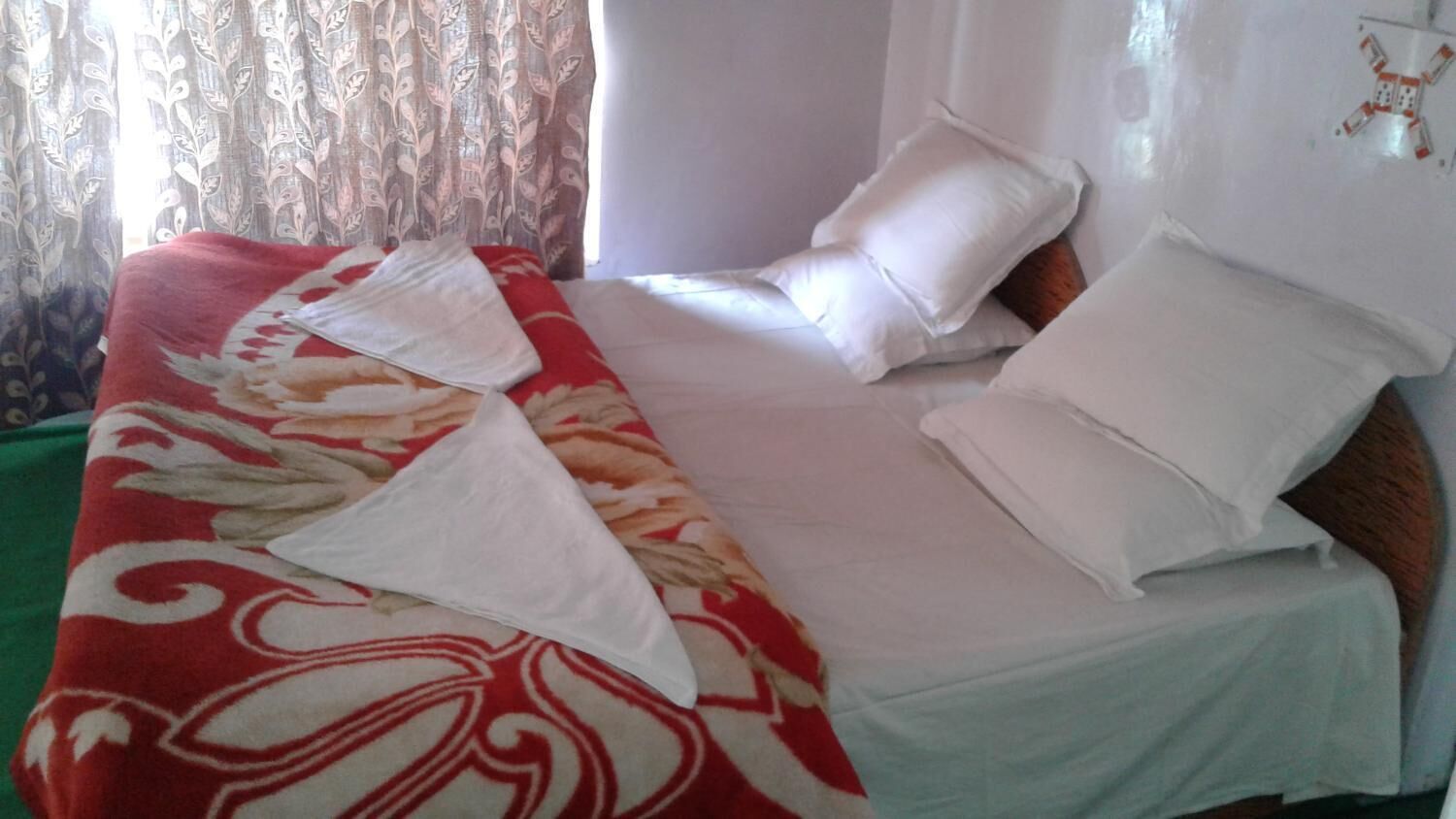 A hotel room with a bed covered in white sheets, a red and white patterned blanket, and a pillow.