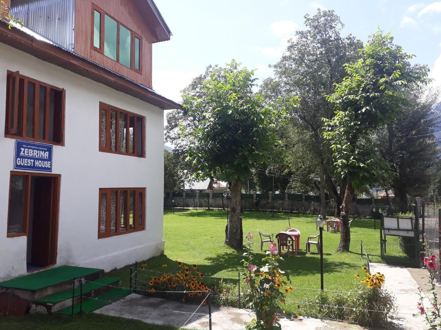 A two-story building labeled "ZEBRINA GUEST HOUSE" with a green lawn, trees, and outdoor furniture.