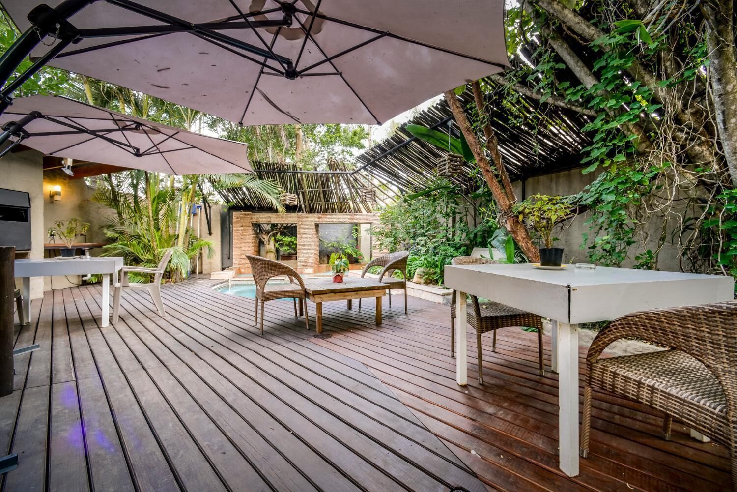 An outdoor patio with wooden flooring, wicker furniture, and a pool area.