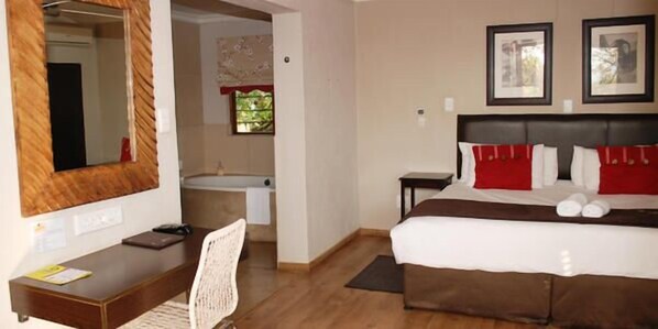 A hotel room with a bed, a desk, a chair, a mirror, a window, and a bathroom.