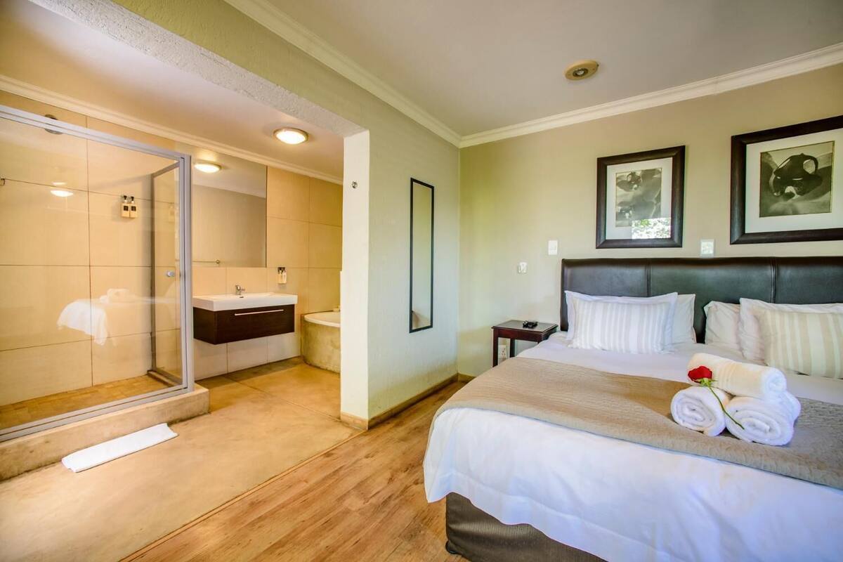 A hotel room with a bed, a bedside table, a nightstand, a mirror, and a bathroom with a shower and sink.