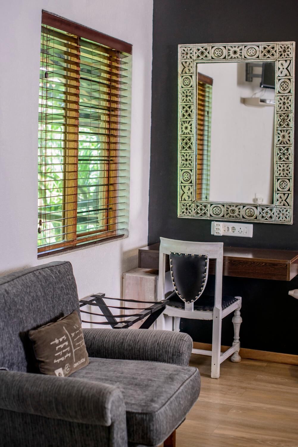 A room with a grey sofa, a white chair, a wooden dresser, and a large mirror with a decorative frame.