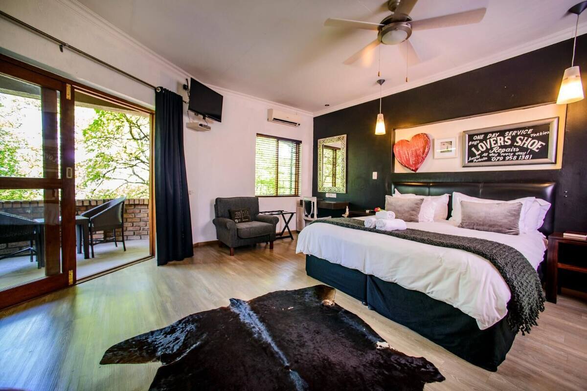 A bedroom with a bed, a chair, a table, a TV, and a view of the outdoors.