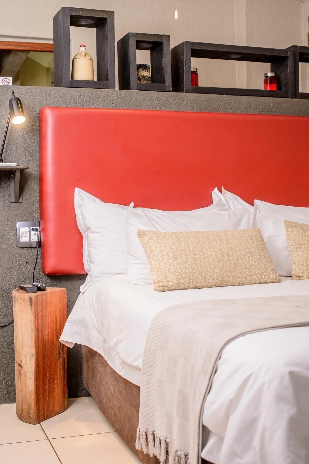 A modern bedroom with a red headboard, white bedding, and a wooden nightstand.
