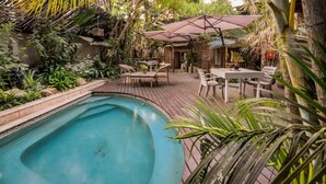 Una piscina rodeada de exuberante vegetación, terraza de madera y zona de estar al aire libre.