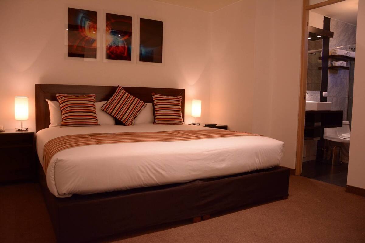 A hotel room with a large bed, two bedside tables, and a nightstand. There are three framed pictures on the wall above the bed.