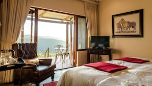 A hotel room with a bed, a TV, a desk with a kettle, and a view of the outdoors. - The Hilton Bush Lodge (Hilton)