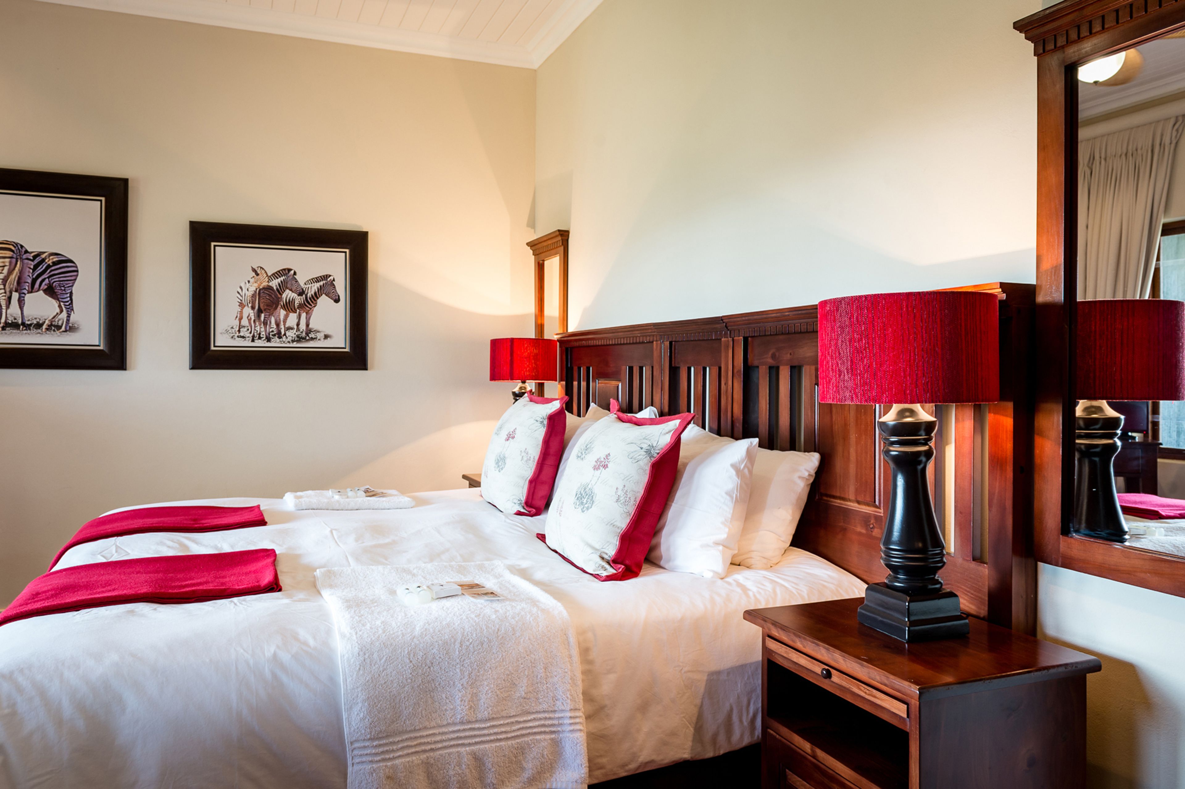 A neatly made bed with white linens and red accents, a wooden headboard, and two framed zebra pictures on the wall.