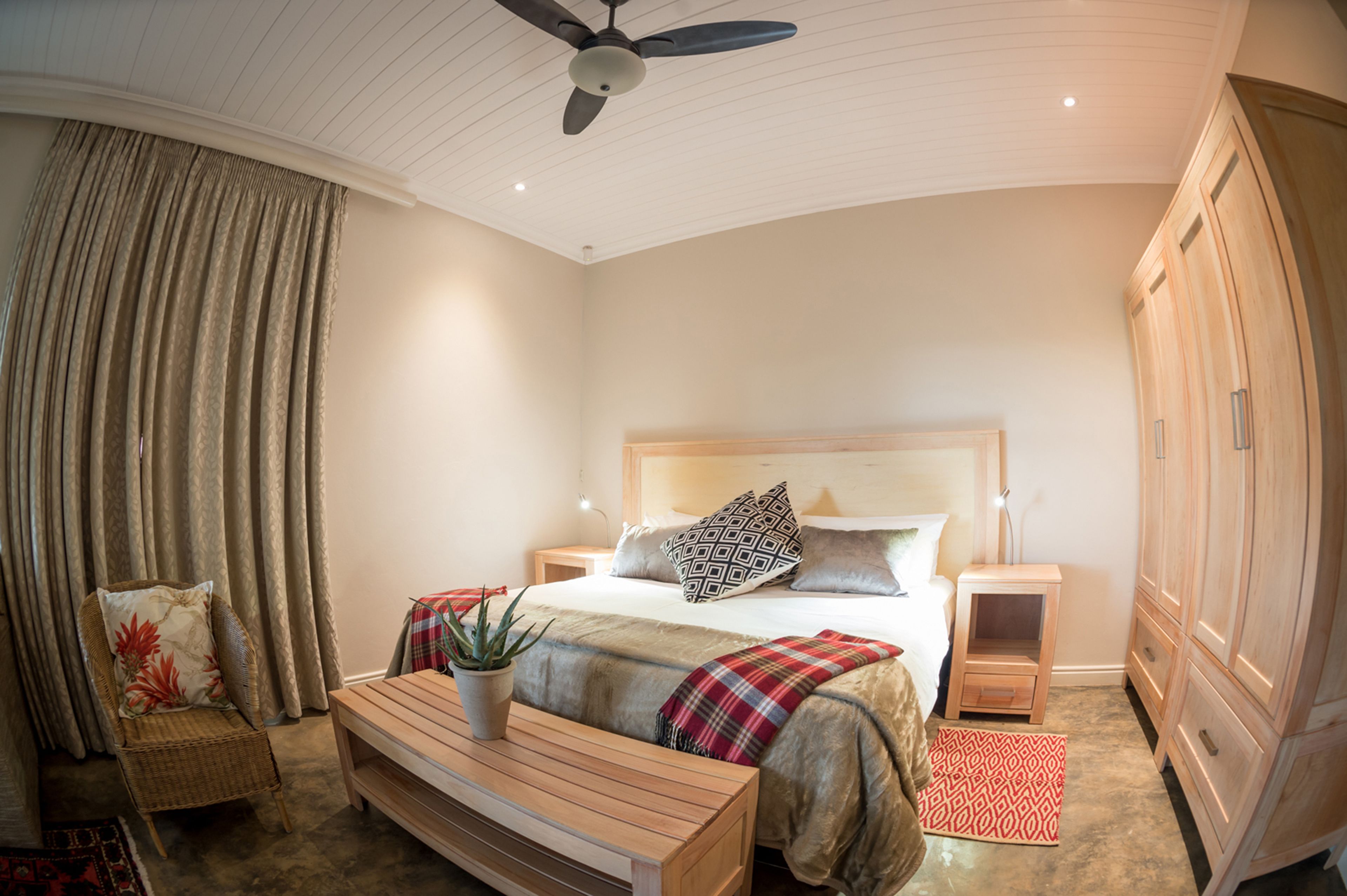 Ein Schlafzimmer mit einem Bett, Nachttischen, einem Deckenventilator, einem Kleiderschrank und einem kleinen Tisch mit einer Pflanze.