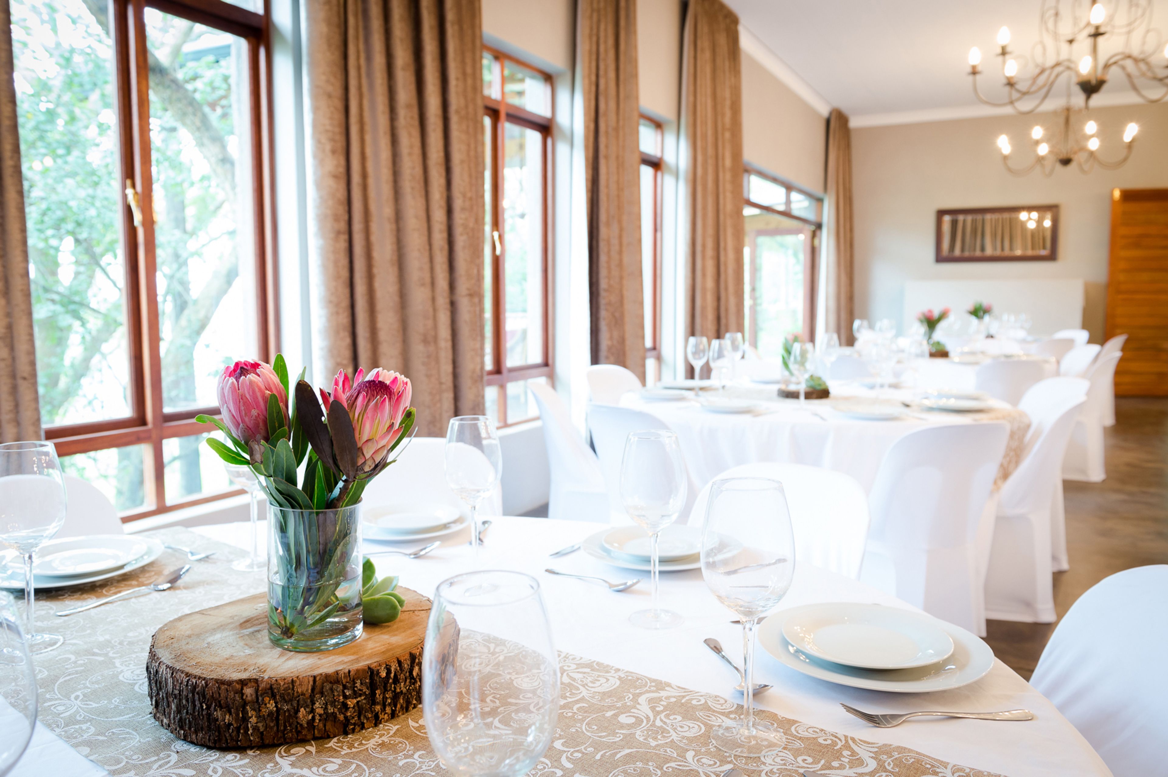 A dining area with tables set for a meal, large windows, and a chandelier.