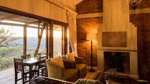A cozy living room with a fireplace, a dining table with chairs, and a view of the outdoors. - The Hilton Bush Lodge (Hilton)