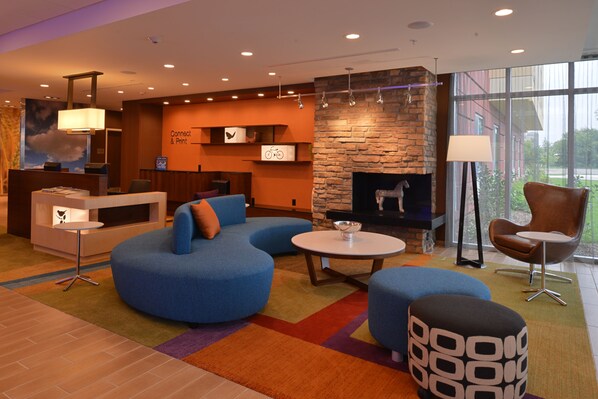 Een moderne hotel lobby met een stenen openhaard, blauwe zitplaatsen en een receptiebalie.