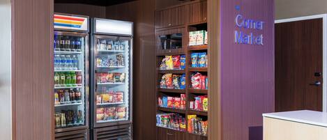 A corner market with refrigerated beverage dispensers and shelves stocked with snacks and packaged goods.