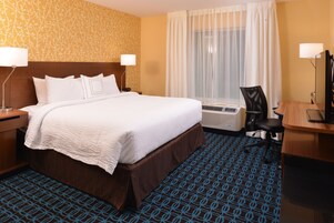 A hotel room with a large bed, a desk, a chair, and a window with curtains.