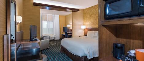 Una habitación de hotel con cama, escritorio, televisor y microondas.