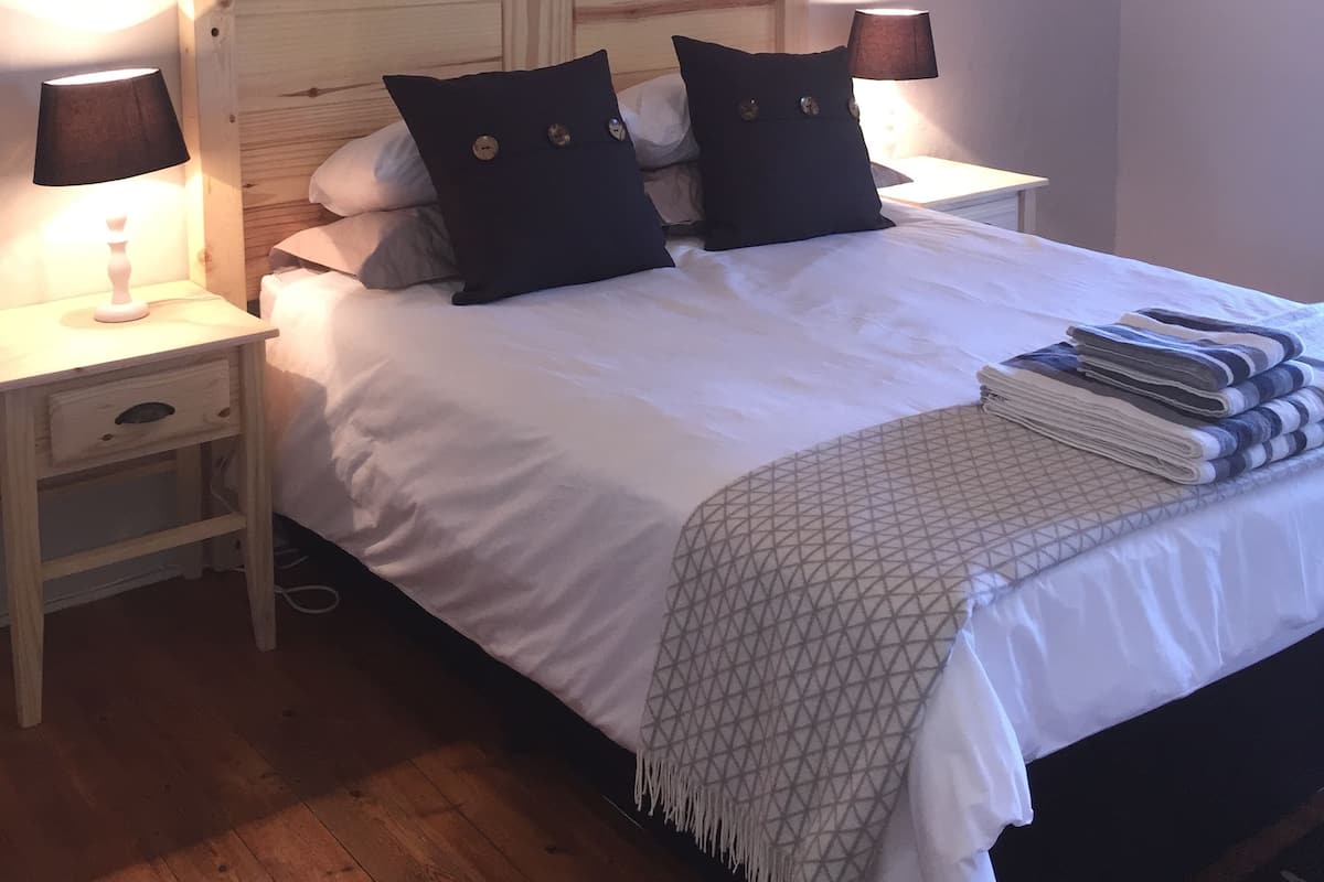 A neatly made bed with a wooden headboard, two bedside tables with lamps, and a bedside shelf.