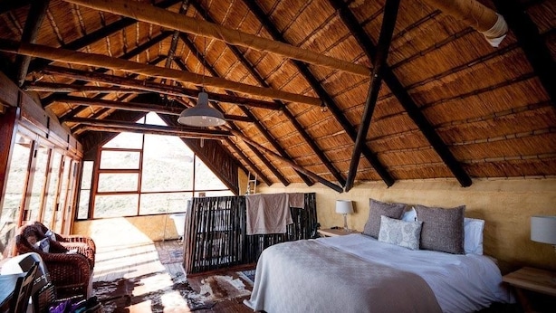 Una habitación rústica con techo de madera alto, una cama con almohadas, una silla y una mesa.