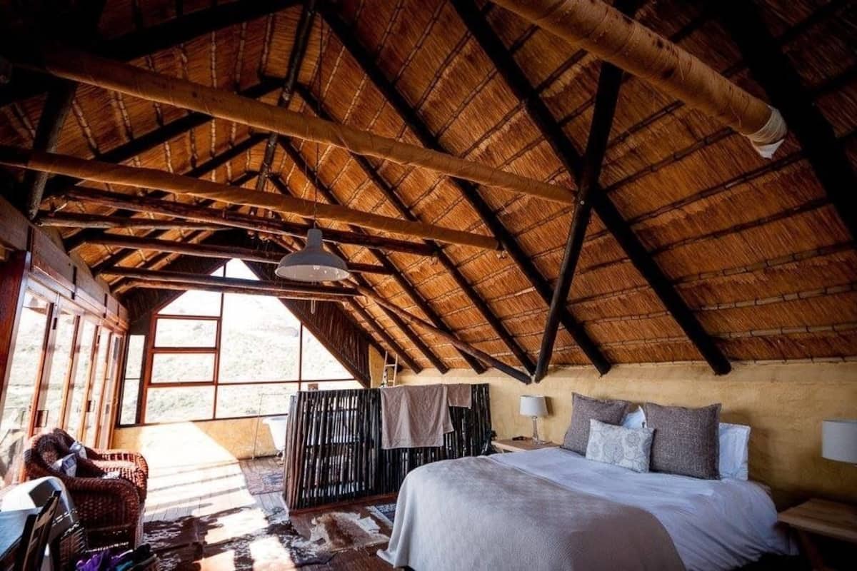 A rustic room with a high wooden ceiling, a bed with pillows, a chair, and a table.