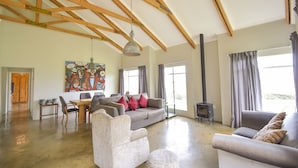 Un salón comedor amplio con techo alto, vigas de madera, chimenea y ventanas grandes.