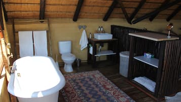 A rustic bathroom with a bathtub, toilet, sink, and shelves.