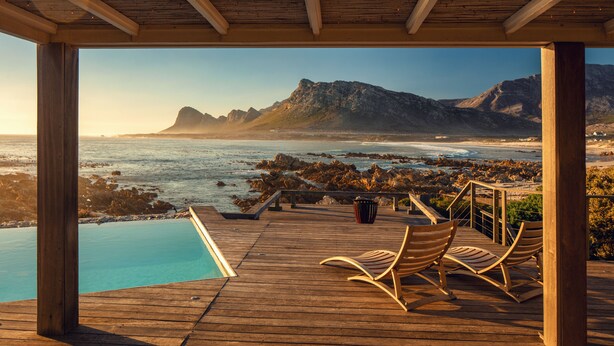 A wooden deck with a pool and lounge chairs overlooking a beach and mountains. - Pringle Bay Villa (Pringle Bay)