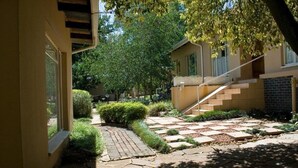 A courtyard with a brick pathway, a small bridge, and a staircase leading to a second floor.