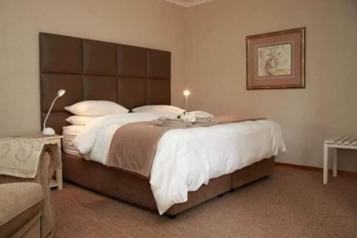 Una cama bien hecha con cabecera, una mesita de noche con lámpara y un cuadro en la pared.