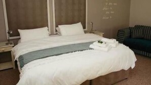 A neatly made bed with white linens and a blue accent, a bedside table with a lamp, and a wall with a motivational quote.