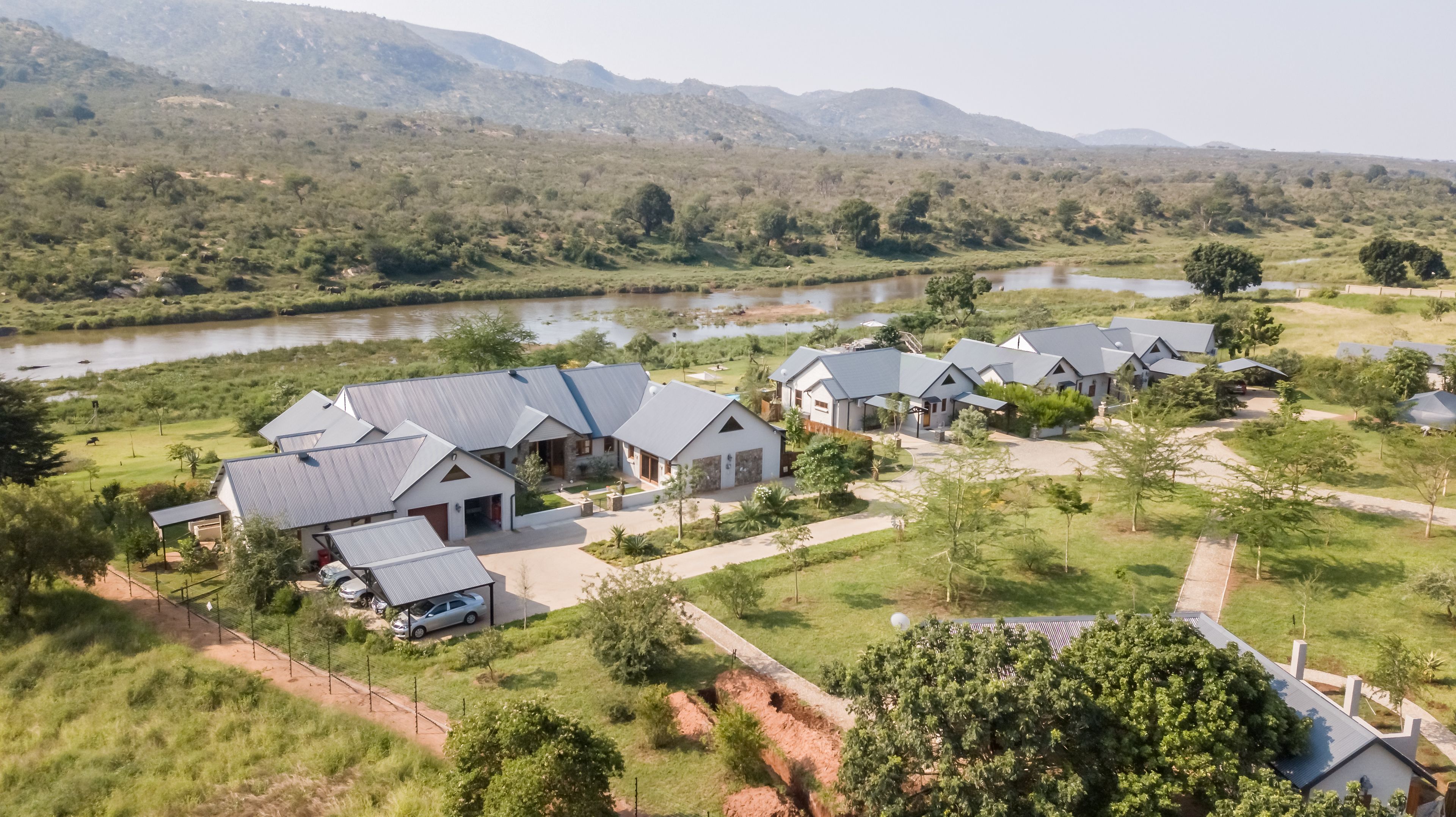 A residential area with multiple houses, a river, and hills in the background.