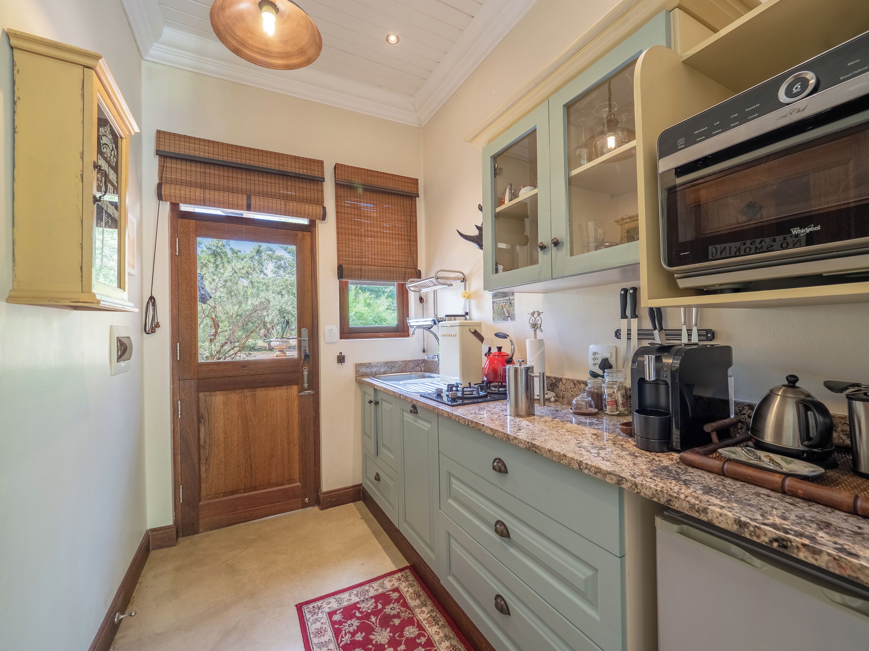 A kitchen with a wooden door, a window with blinds, a countertop with various appliances, and a built-in oven.