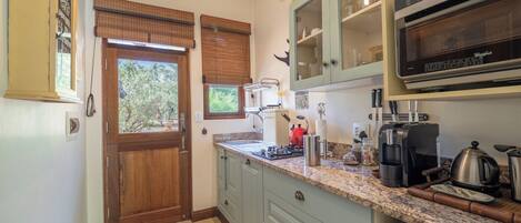 A kitchen with a wooden door, a window with blinds, a countertop with various appliances, and a built-in oven.