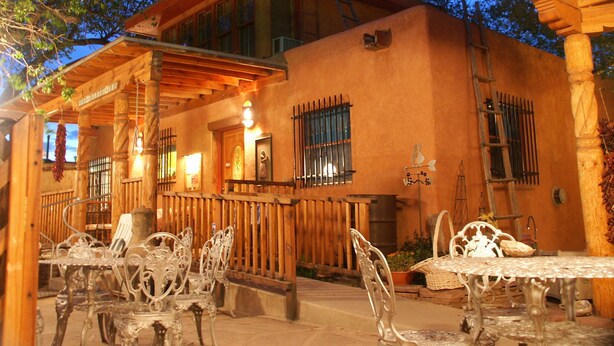 A rustic building with a covered patio, outdoor seating, and a wooden staircase. - Inn at Halona (Zuni)