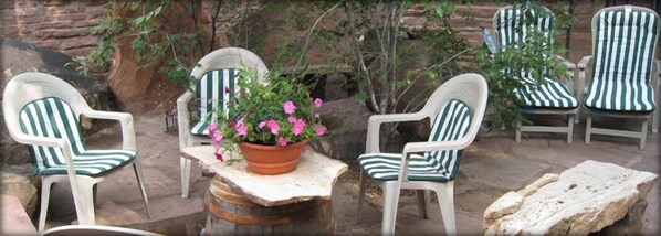 A patio area with four striped chairs, a round table, and a potted plant with pink flowers. - Inn at Halona (Zuni)