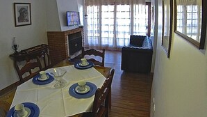 A dining area with a table set for four, a fireplace, and a sofa in the background. - Apartamento dois quartos Capivarí (Campos do Jordão)