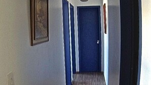 A narrow hallway with wooden flooring, a blue door at the end, and a hanging light fixture. - Apartamento dois quartos Capivarí (Campos do Jordão)